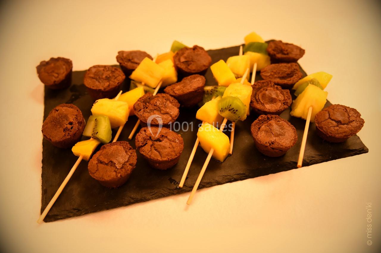 Brochettes composées de morceaux de fruits frais et de mini brownies, présentées sur une ardoise noire.