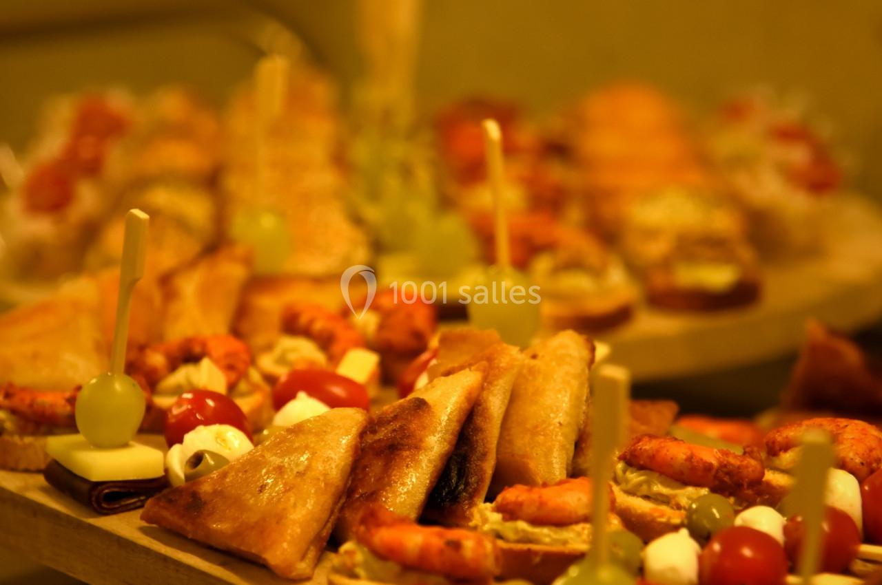 Plateaux de tapas variés avec brochettes, feuilletés, crevettes et autres amuse-bouches disposés sur une table en bois.