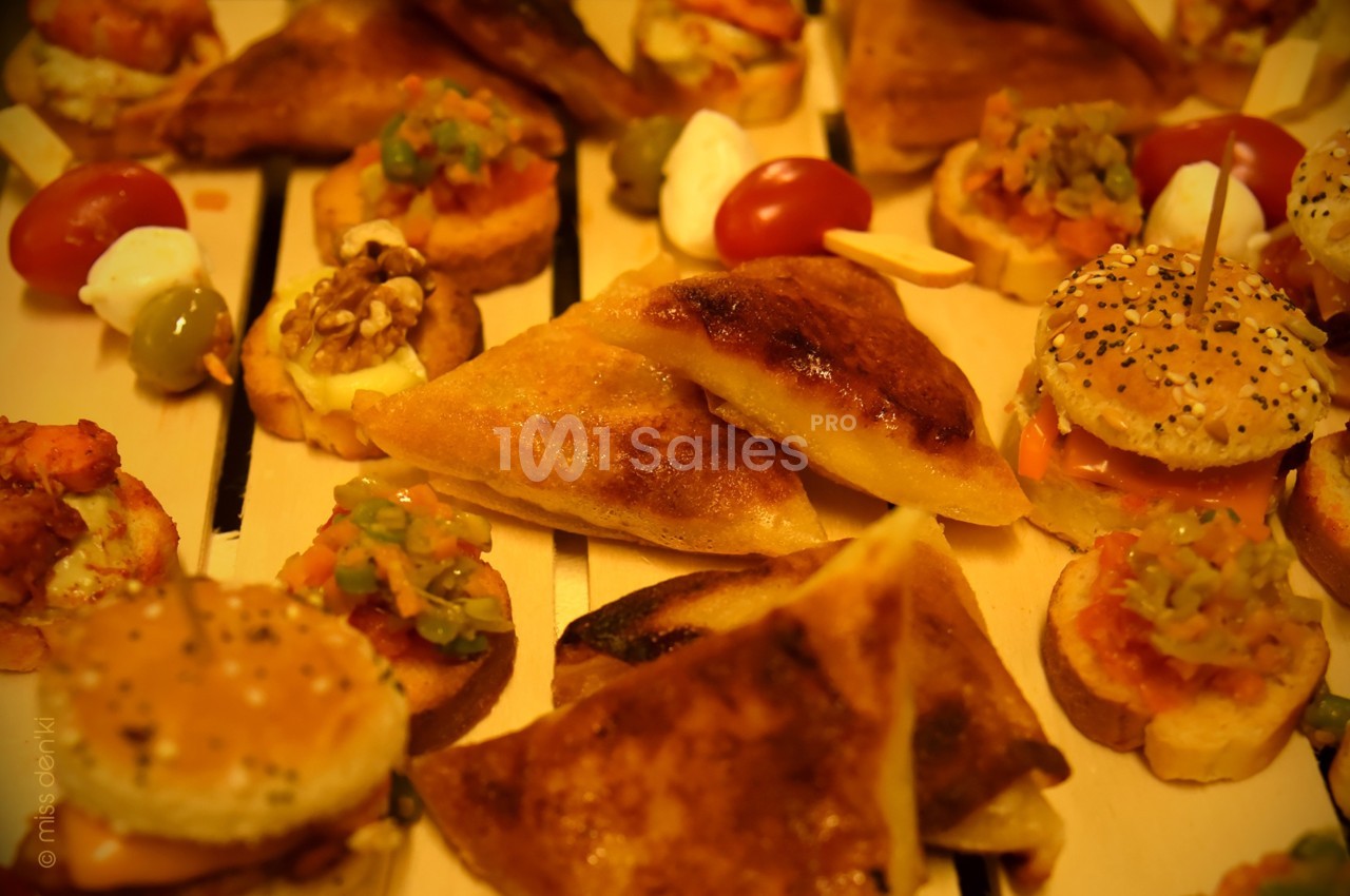 Assortiment de bouchées apéritives variées, incluant mini-burgers, feuilletés et canapés sur une table en bois.