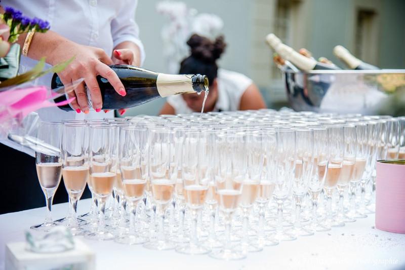 Une personne verse du champagne dans des flûtes alignées sur une table lors d'un événement en extérieur.