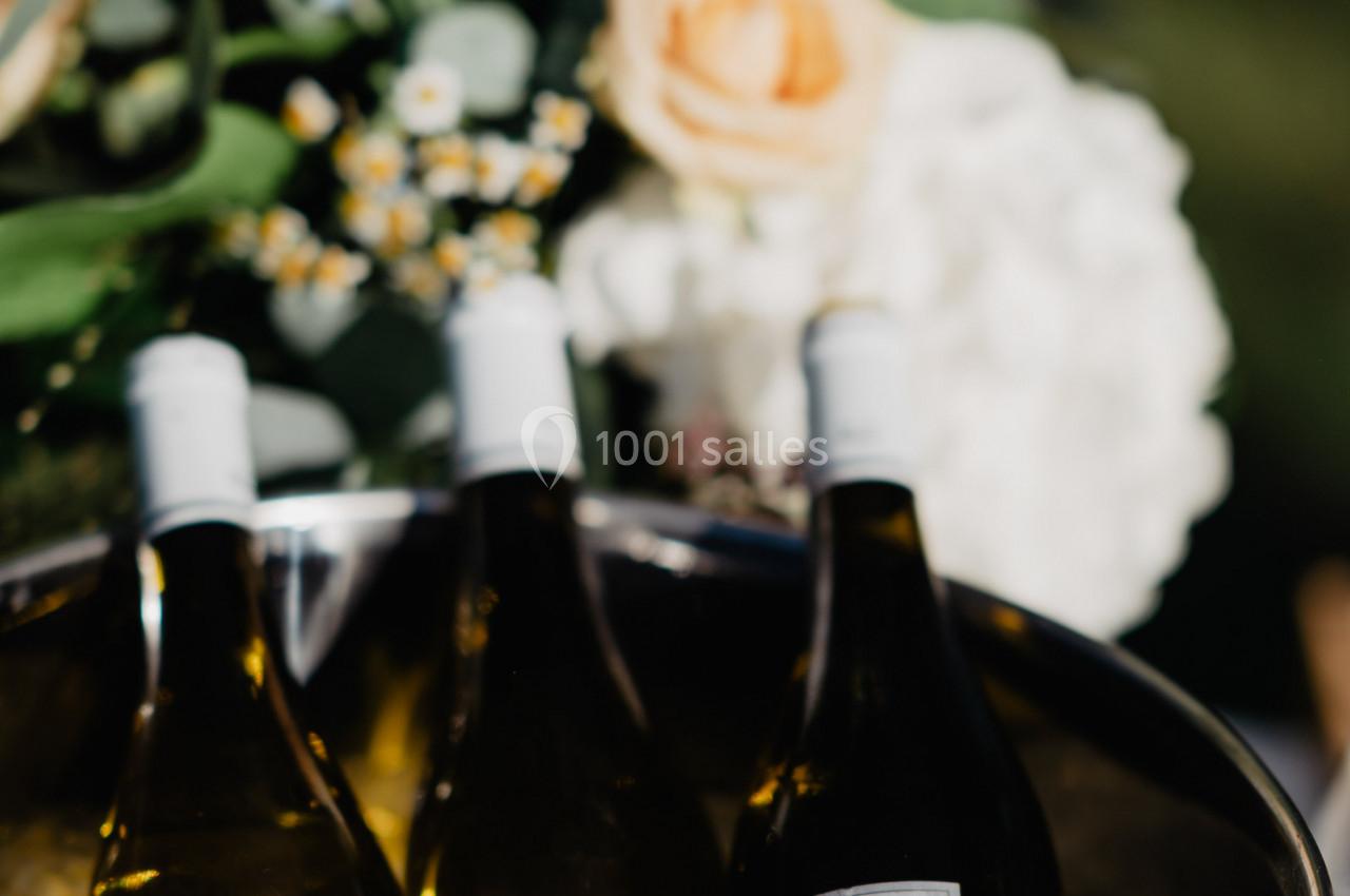 Bouteilles de vin blanc refroidissant dans un seau rempli de glace, avec des fleurs en arrière-plan.