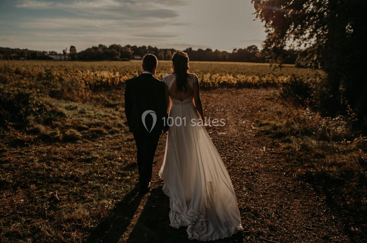 Un couple en tenue de mariage marche sur un chemin rural au coucher du soleil, entouré de végétation.