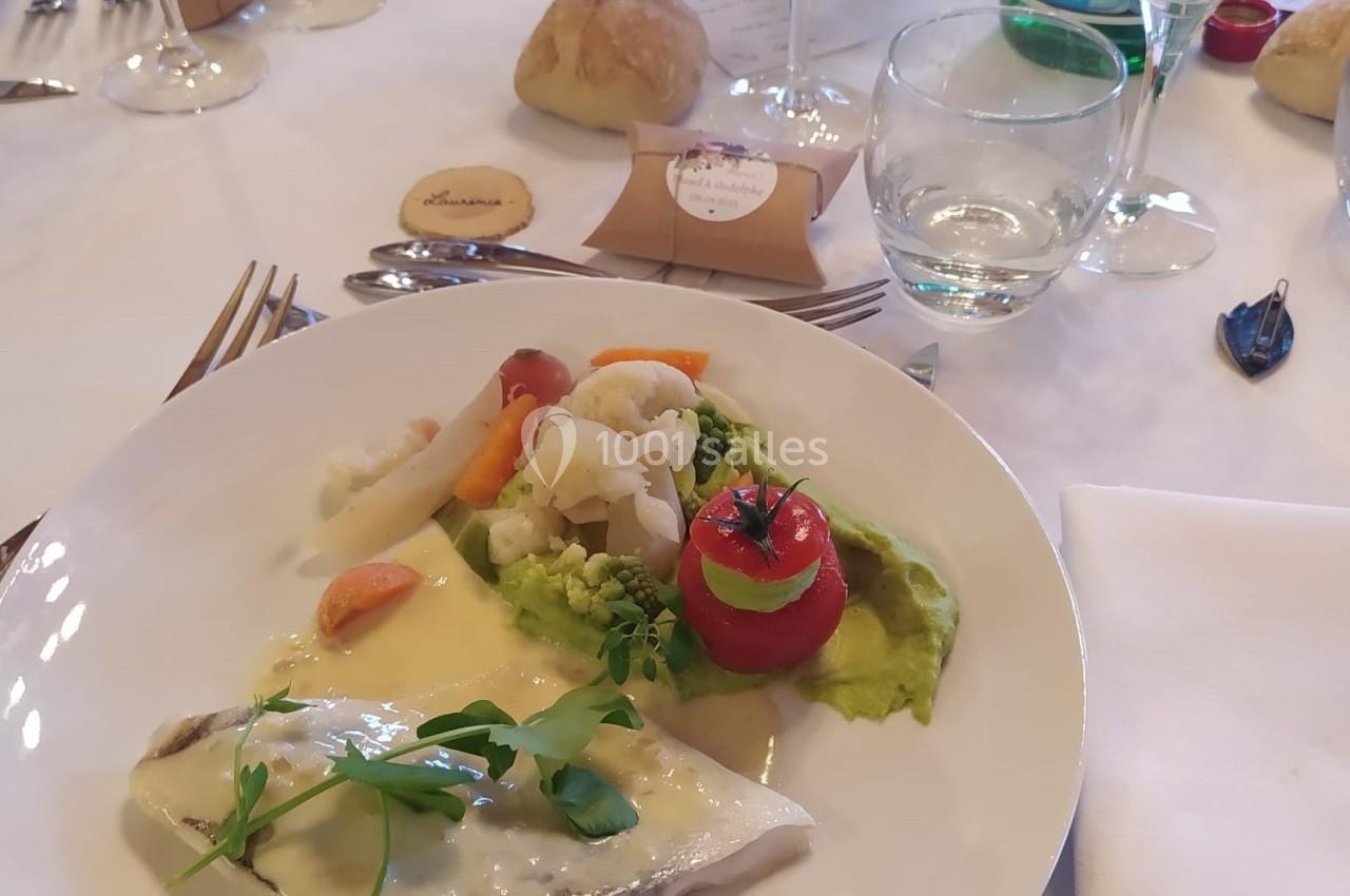 Assiette de poisson avec sauce, légumes variés, purée verte, et décoration, sur une table dressée pour un repas.