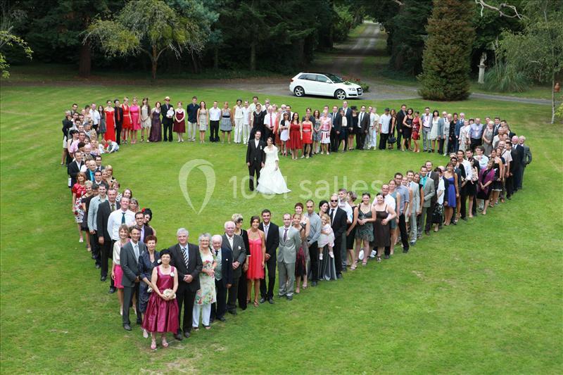 Un groupe de personnes formant un cœur autour d'un couple de mariés sur une pelouse verte.