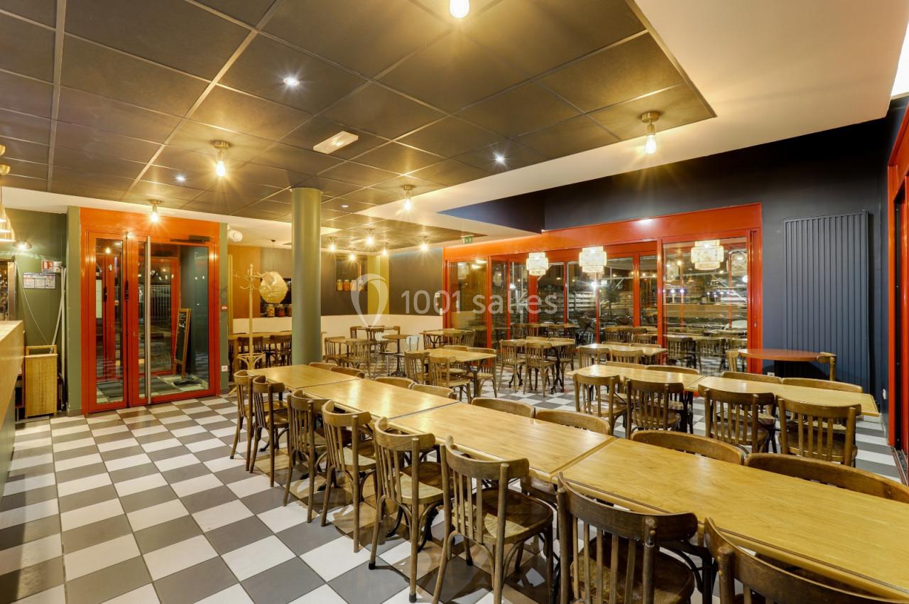 Salle de restaurant avec tables en bois, chaises assorties et éclairage chaleureux, sol en damier noir et blanc.