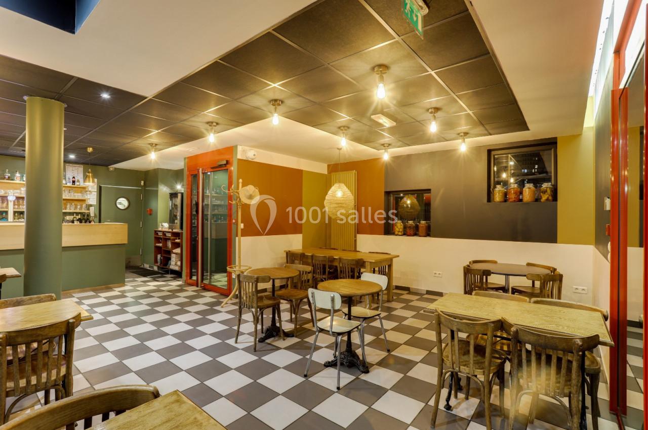 Salle de restaurant vide avec tables en bois, sol à carreaux, éclairage suspendu et comptoir en arrière-plan.