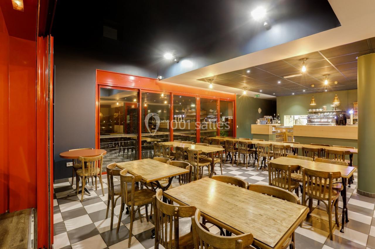 Salle de restaurant moderne avec tables en bois, chaises assorties et comptoir lumineux en arrière-plan.
