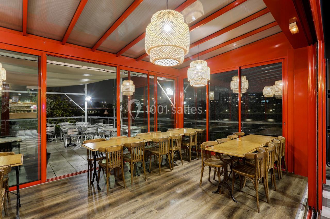 Salle de restaurant lumineuse avec des tables en bois, chaises assorties et suspensions en osier, donnant sur une terrasse…
