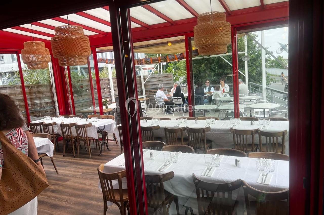 Salle de restaurant lumineuse avec tables dressées, vue sur une terrasse extérieure et des clients attablés.