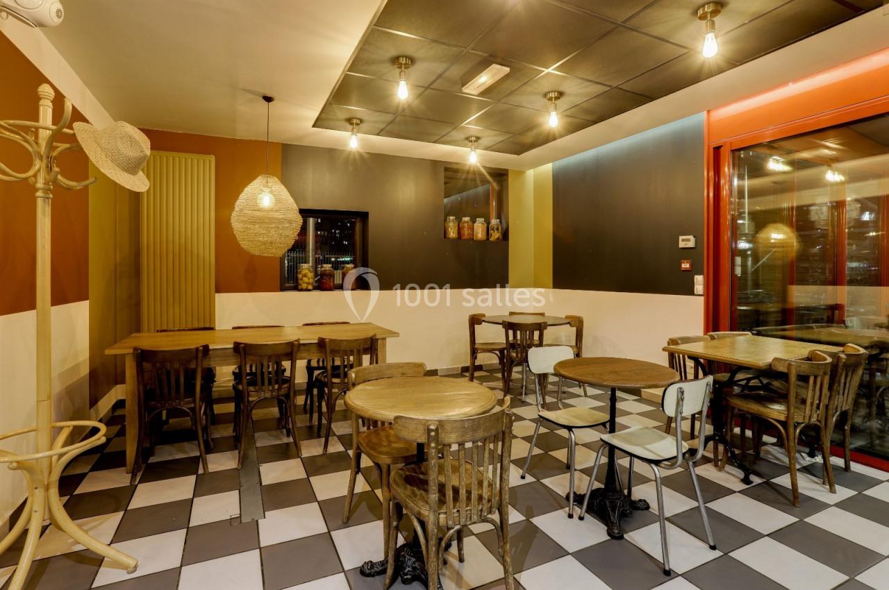 Salle de restaurant avec tables en bois, chaises assorties, sol à carreaux noirs et blancs, éclairage suspendu.