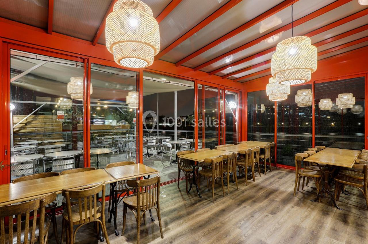 Salle de restaurant lumineuse avec tables en bois, chaises assorties et grandes baies vitrées donnant sur une terrasse.