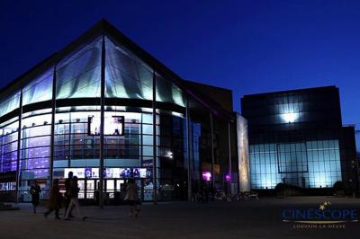 Façade éclairée d'un cinéma moderne en soirée, avec quelques passants devant l'entrée.