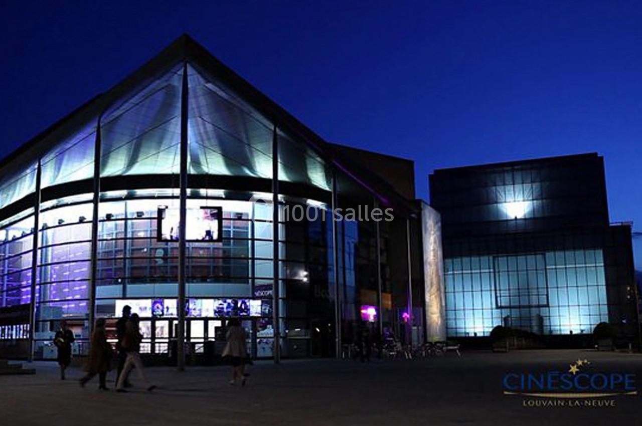 Façade éclairée d'un cinéma moderne en soirée, avec quelques passants devant l'entrée.