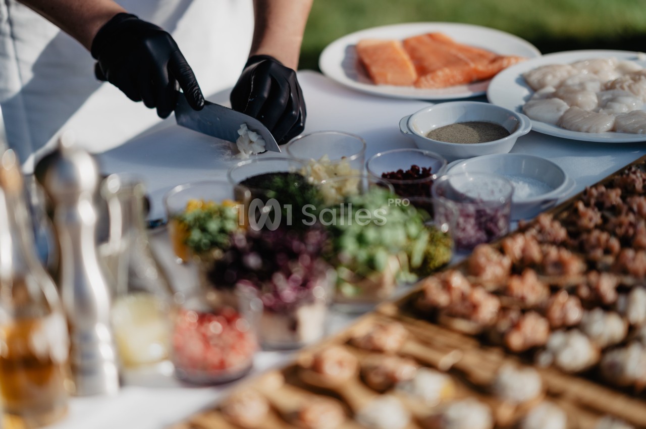Un chef découpe des oignons sur une table garnie d'ingrédients et de plats, dont du saumon et des fruits de mer.