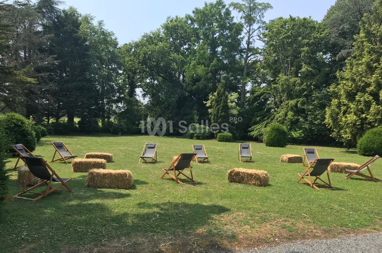 Chaises longues et bottes de paille disposées en cercle sur une pelouse entourée d'arbres.