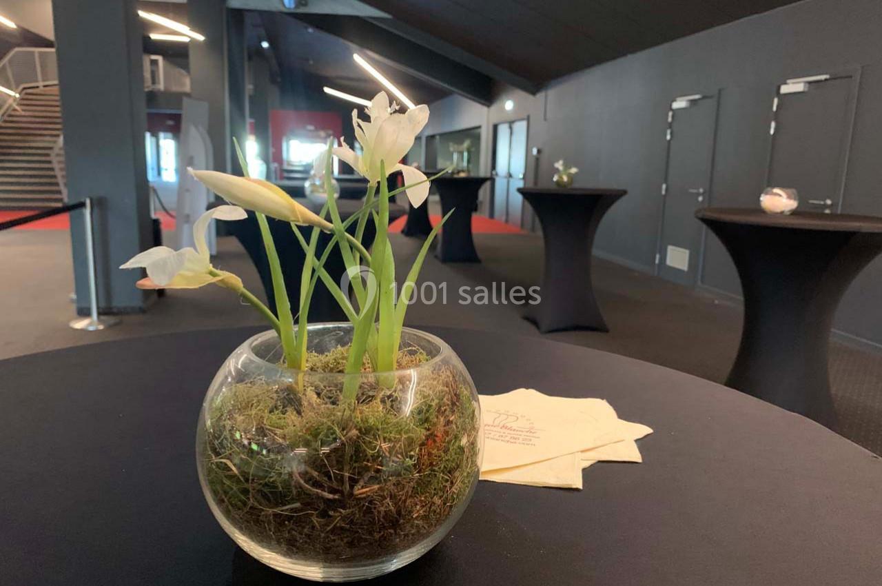 Vase rond avec des fleurs blanches et de la mousse, posé sur une table noire dans une salle moderne.