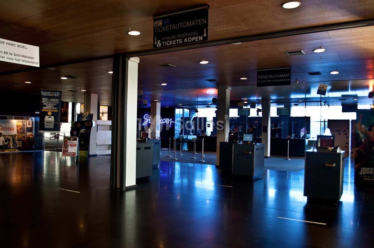 Hall d'entrée d'un cinéma avec bornes automatiques, panneaux d'information et guichets visibles au fond.