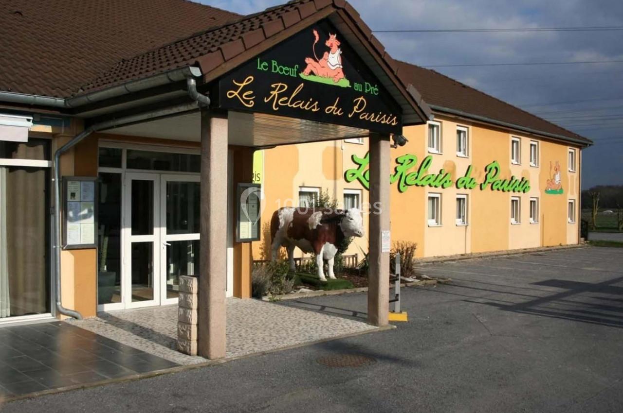 Façade d'un restaurant avec une statue de vache devant l'entrée, bâtiment beige et enseigne visible.