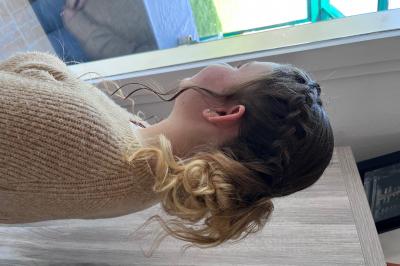 Miniature Hair by elle  #6 Femme de dos avec des cheveux blonds coiffés en tresse et chignon, portant un pull beige près d'une fenêtre.