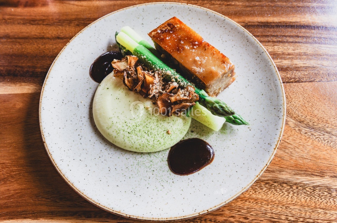 Assiette gastronomique avec viande, purée, asperges, sauce et garniture de champignons sur une table en bois.