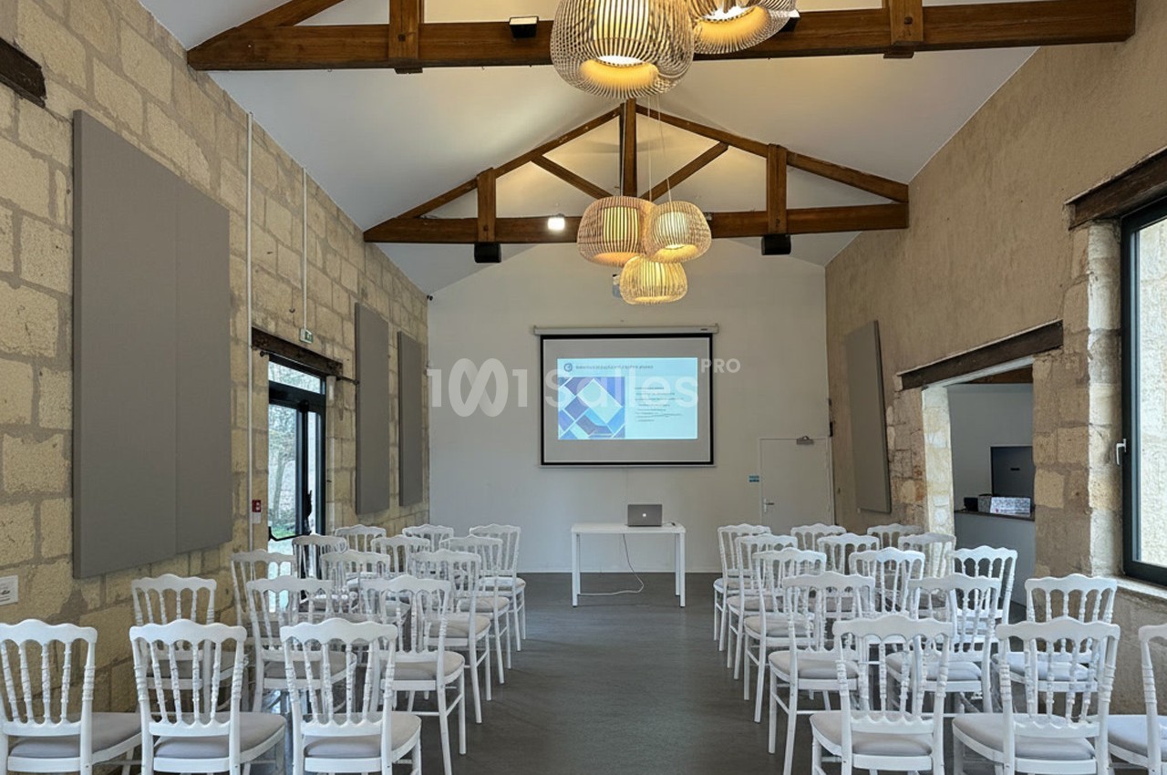 Salle de conférence lumineuse avec des chaises blanches alignées face à un écran de projection et un ordinateur portable.