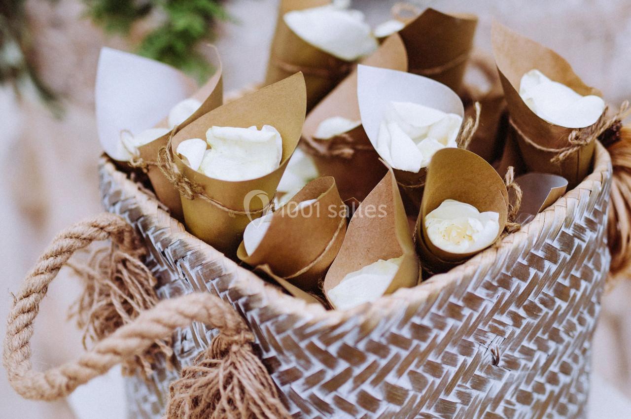 Cônes en papier kraft remplis de pétales blancs disposés dans un panier tressé avec des poignées en corde.