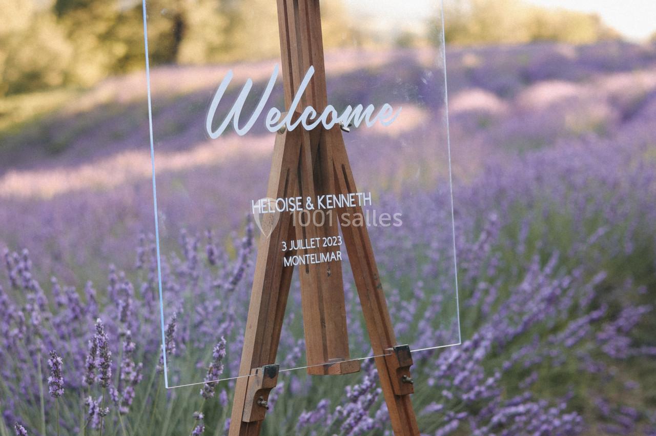 Chevalet en bois avec un panneau transparent indiquant un message de bienvenue, placé dans un champ de lavande.
