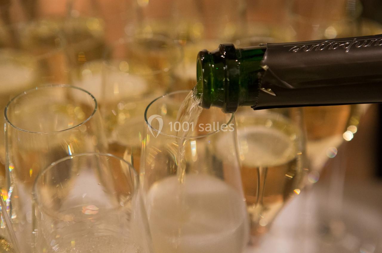 Un verre de champagne est rempli depuis une bouteille, entouré de flûtes déjà servies.
