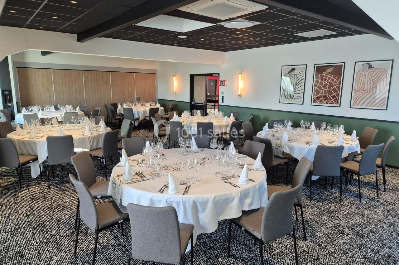 Salle de réception avec tables rondes dressées, nappes blanches, chaises grises et décorations murales modernes.