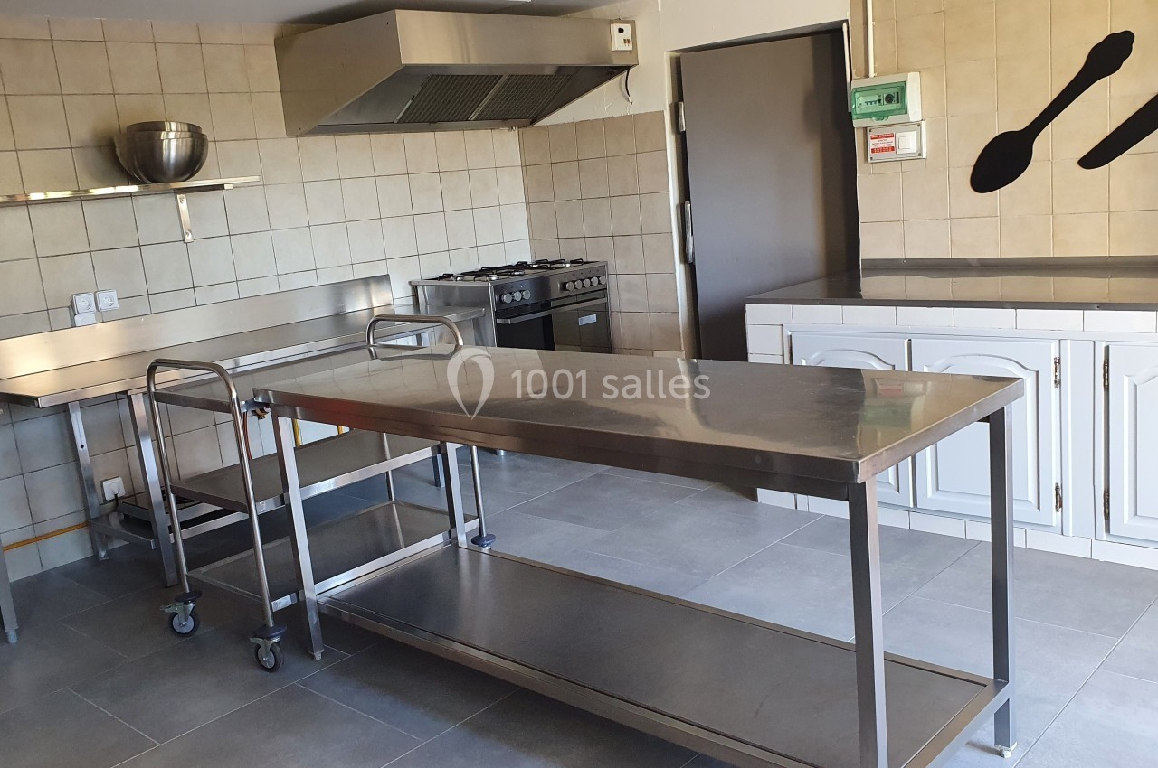 Cuisine professionnelle avec plans de travail en inox, étagères murales, cuisinière et ustensiles accrochés au mur.