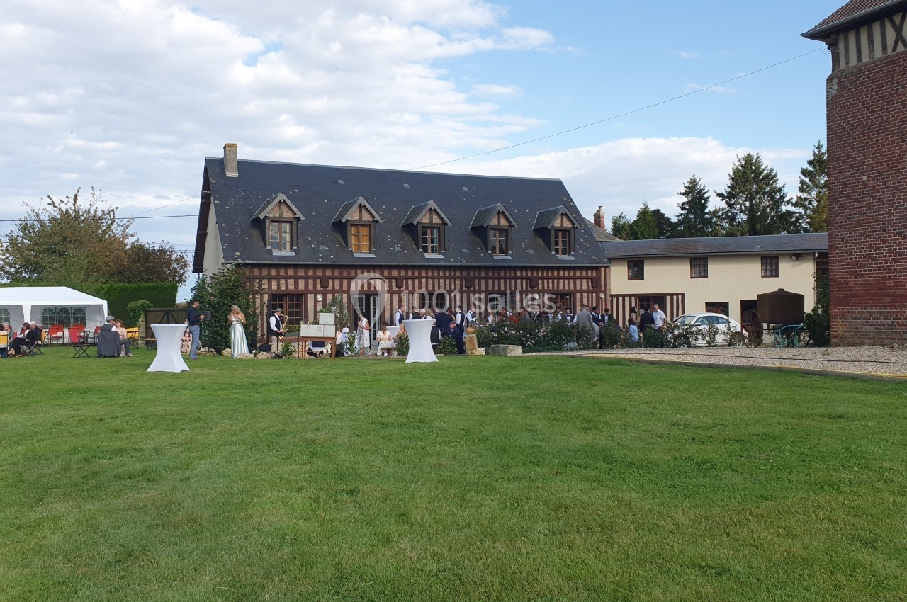Vue d'une grande maison à colombages avec un jardin, des invités rassemblés et des tables en extérieur.