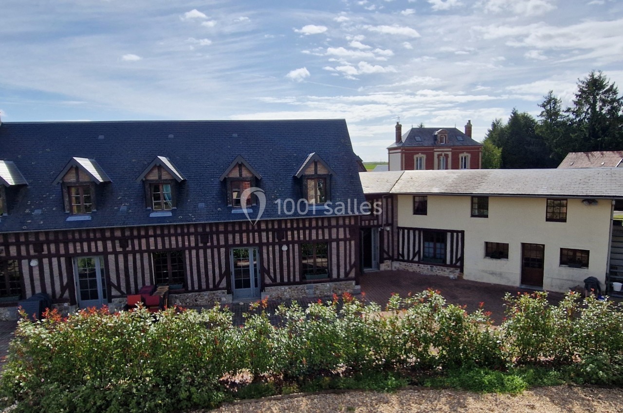 Bâtiments à colombages et maison en arrière-plan, entourés de végétation sous un ciel partiellement nuageux.