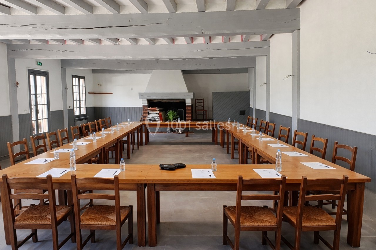 Salle de réunion avec tables disposées en U, chaises en bois, bouteilles d'eau et documents posés sur les tables.