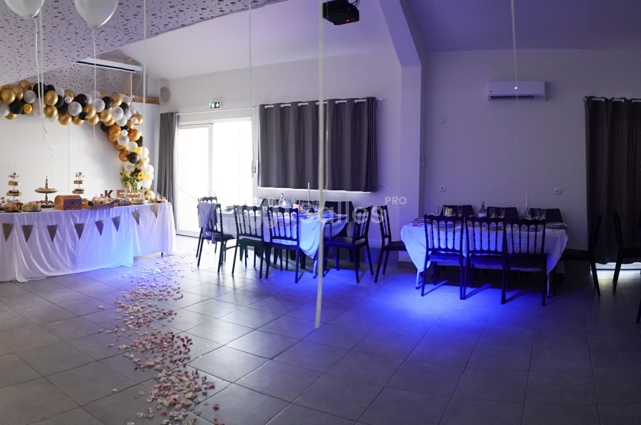 Salle décorée pour un événement avec tables dressées, guirlandes de ballons et pétales au sol.