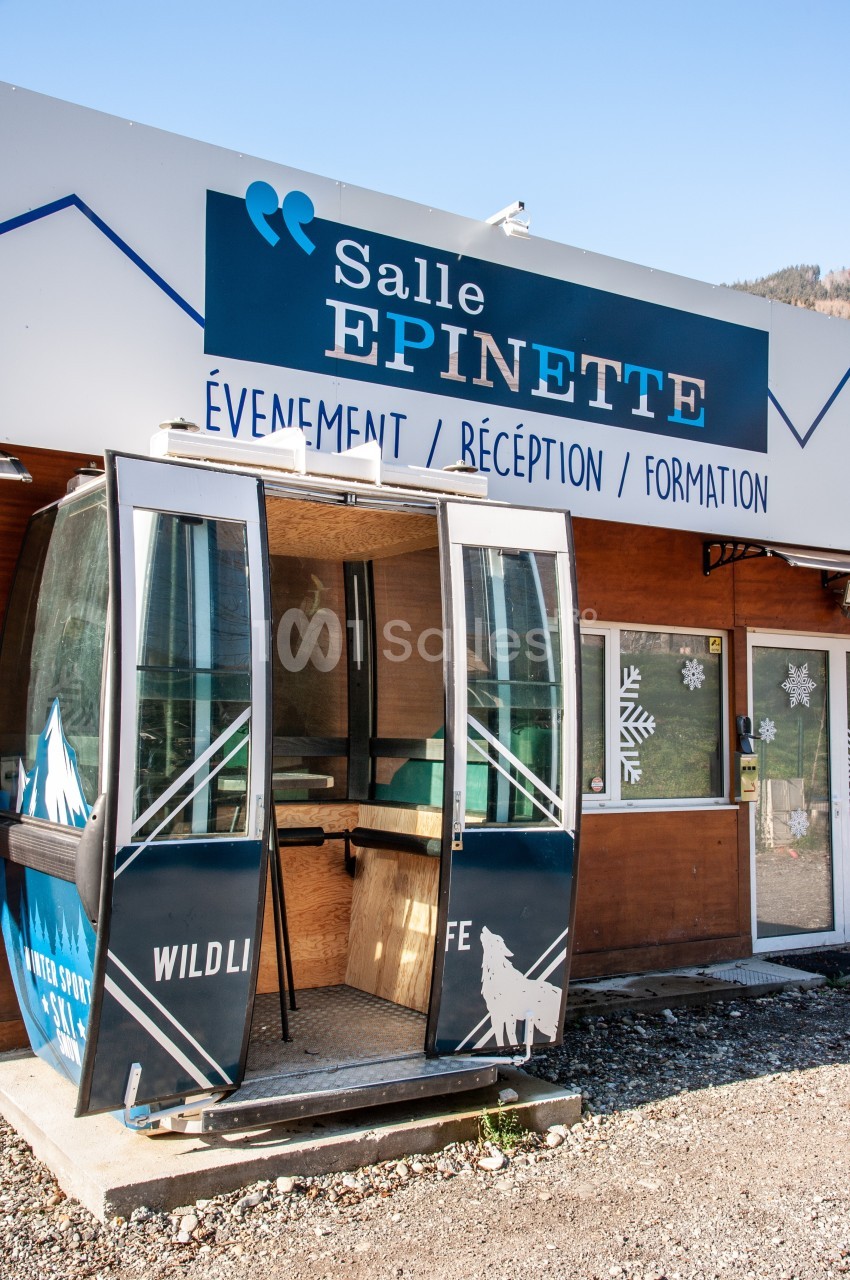 Une ancienne cabine de télécabine transformée en espace d'accueil devant un bâtiment nommé ’Salle Epinette’.