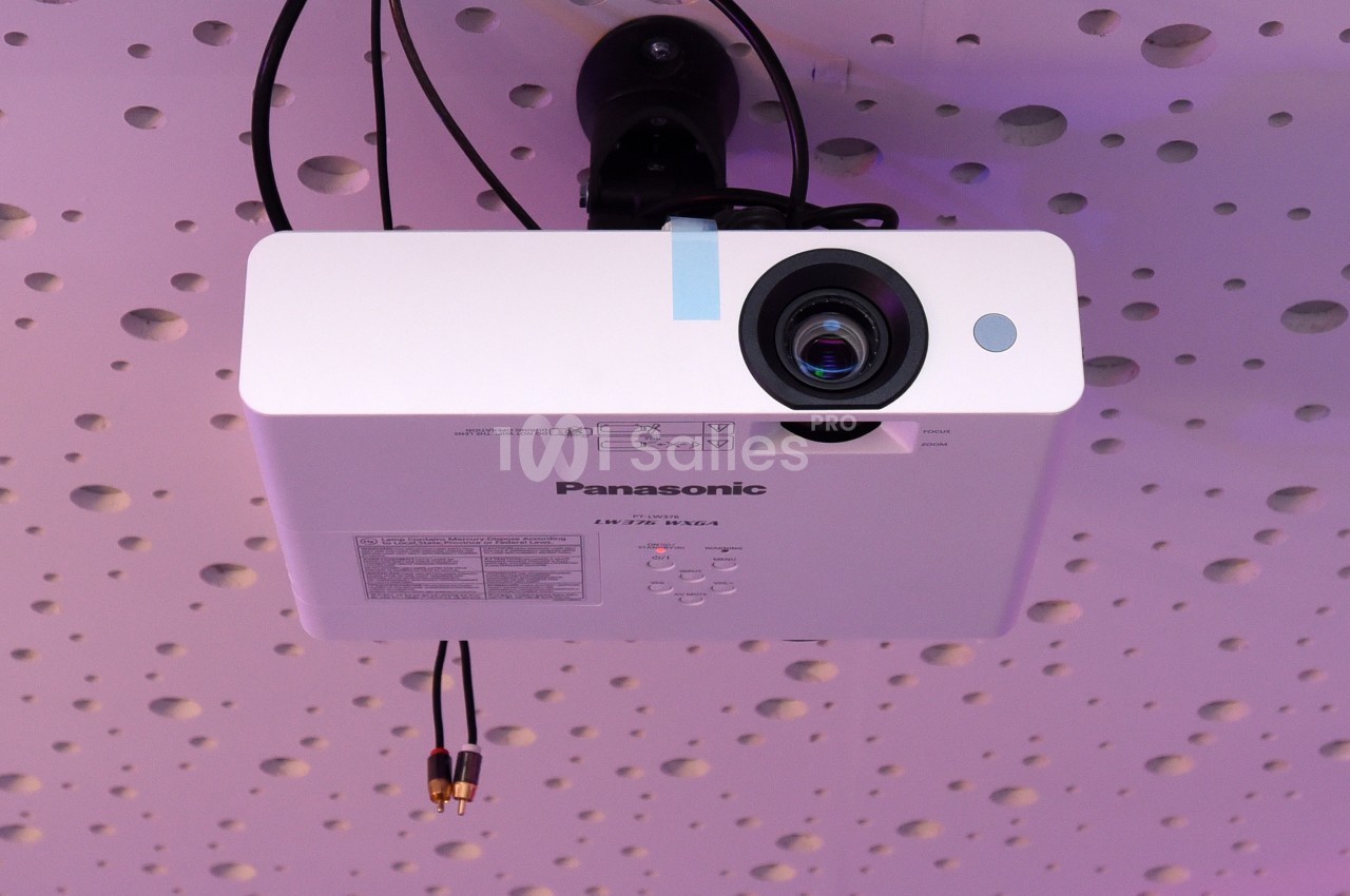Projecteur blanc fixé au plafond perforé, avec câbles connectés et objectif orienté vers le bas.
