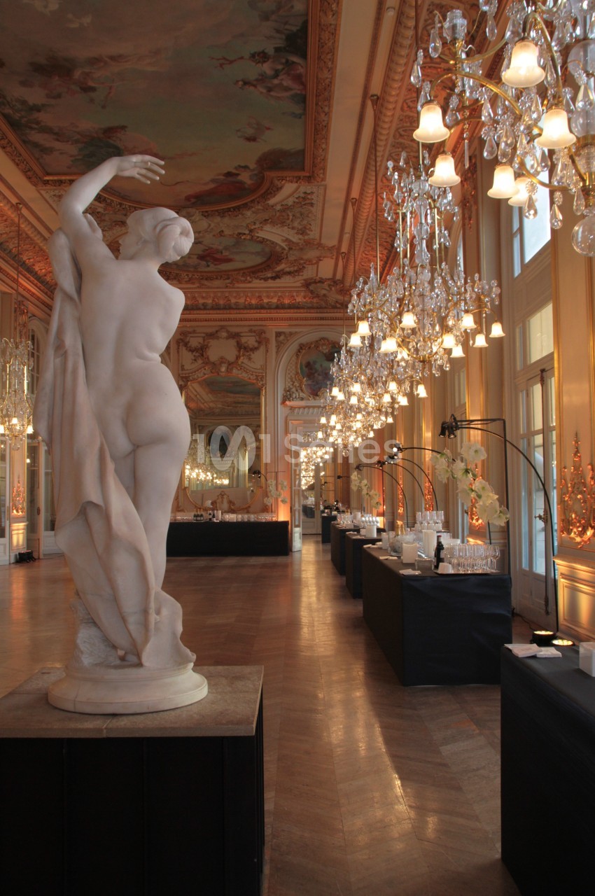 Statue en marbre dans une salle ornée de lustres, fresques au plafond et tables de réception alignées.