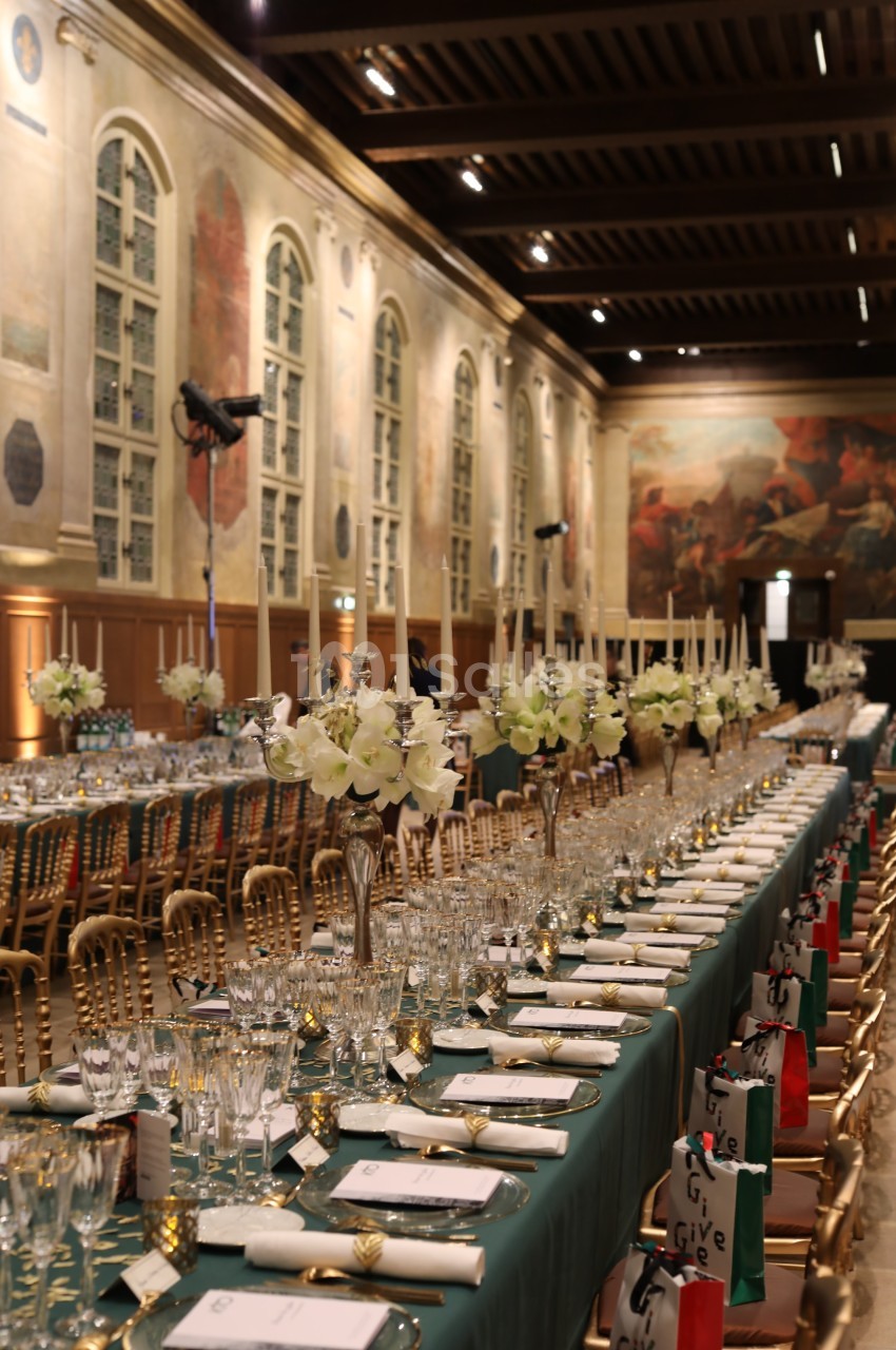 Salle de réception élégante avec longues tables dressées, chandeliers, fleurs blanches et décorations raffinées.