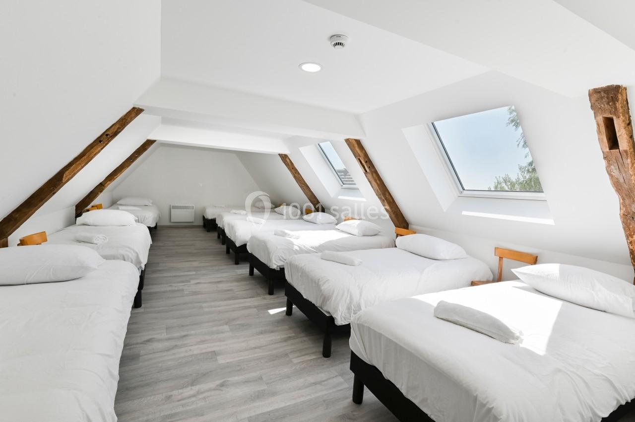 Dortoir lumineux sous combles avec huit lits simples alignés, parquet clair et fenêtres de toit.