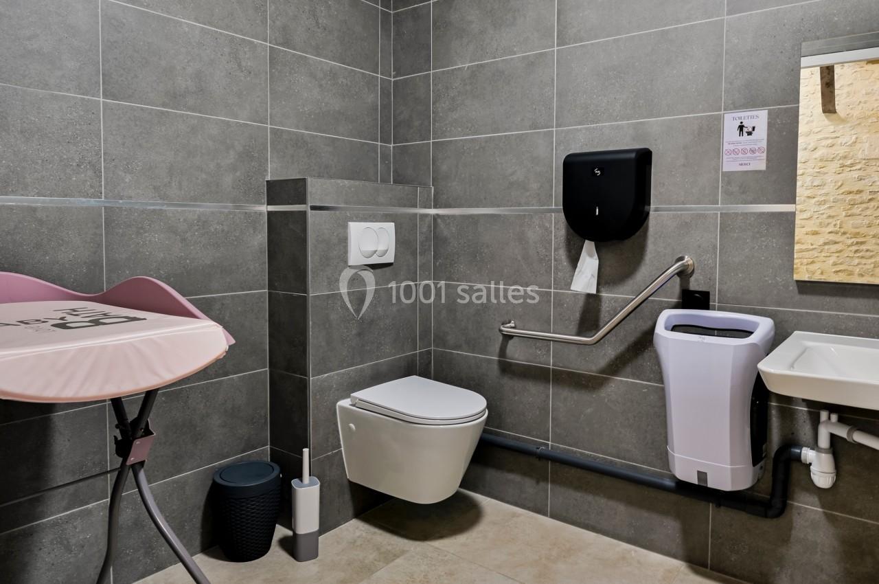 Salle de bain accessible avec toilettes suspendues, barre d'appui, table à langer et lavabo adapté.