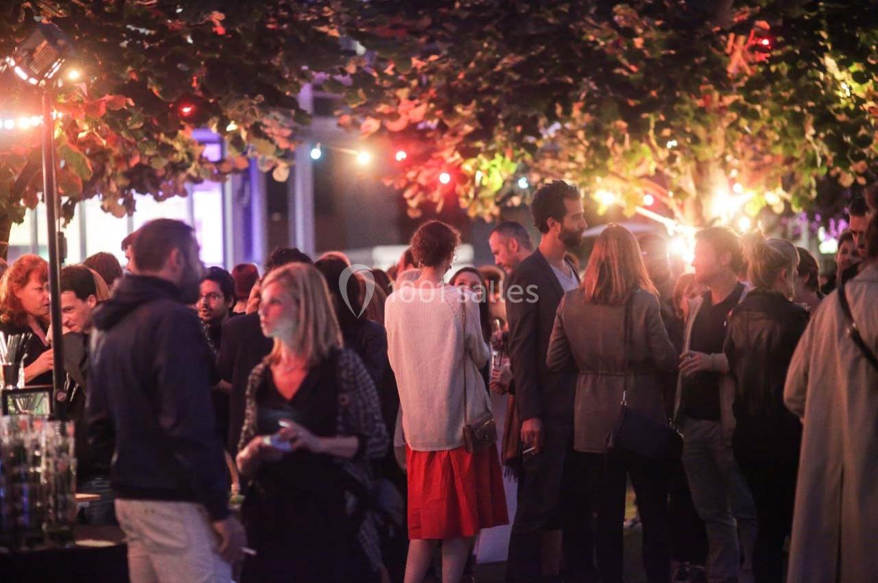 Groupe de personnes discutant sous des arbres décorés de guirlandes lumineuses lors d'un événement en soirée.