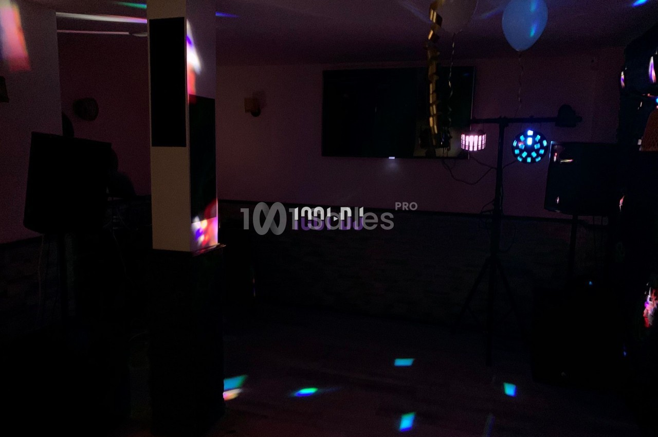 Salle sombre avec jeux de lumières colorées, décorée de ballons et guirlandes, équipée de matériel de sonorisation.