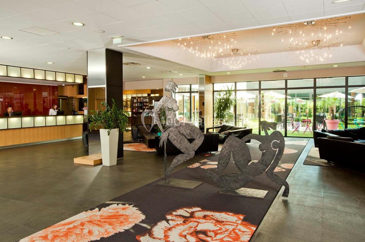 Hall d'entrée spacieux avec une sculpture moderne, des canapés, un comptoir d'accueil et une vue sur un jardin extérieur.