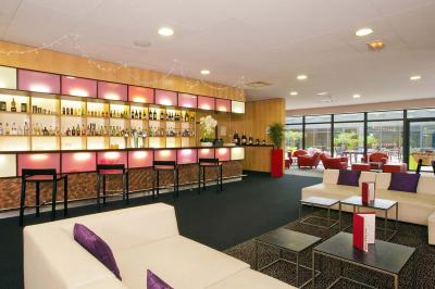 Salle de conférence avec des rangées de chaises grises et jaunes, une scène et une voiture en arrière-plan.