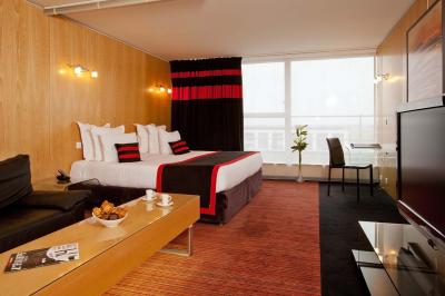 Salle de conférence avec des rangées de chaises grises et jaunes, une scène et une voiture en arrière-plan.