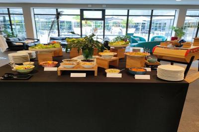 Salle de conférence avec des rangées de chaises grises et jaunes, une scène et une voiture en arrière-plan.