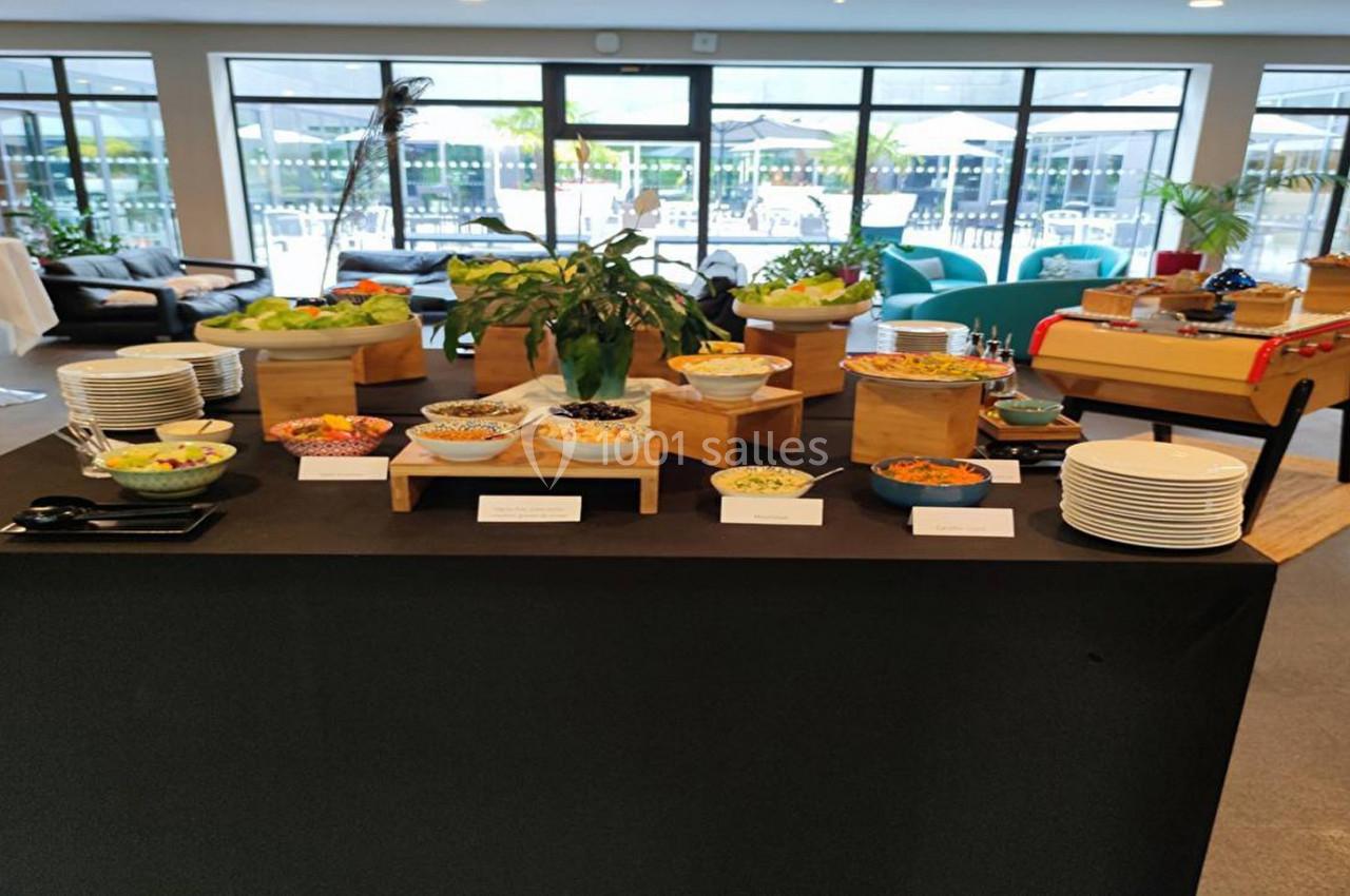 Buffet varié avec salades, condiments et plats disposés sur une table noire dans une salle lumineuse.