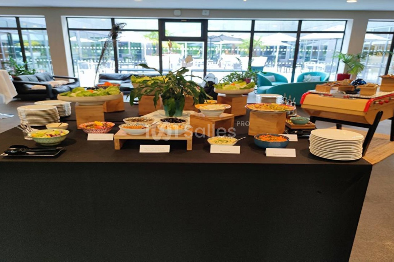 Buffet varié avec salades, condiments et plats disposés sur une table noire dans une salle lumineuse.