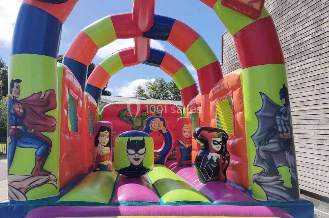 Structure gonflable colorée avec des personnages de super-héros, installée en extérieur près d'un bâtiment en bois.