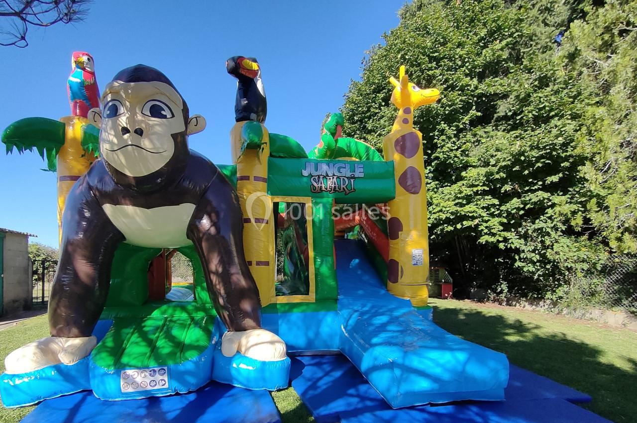Structure gonflable colorée sur le thème de la jungle avec un gorille géant, des animaux et un toboggan, située en extérieur.